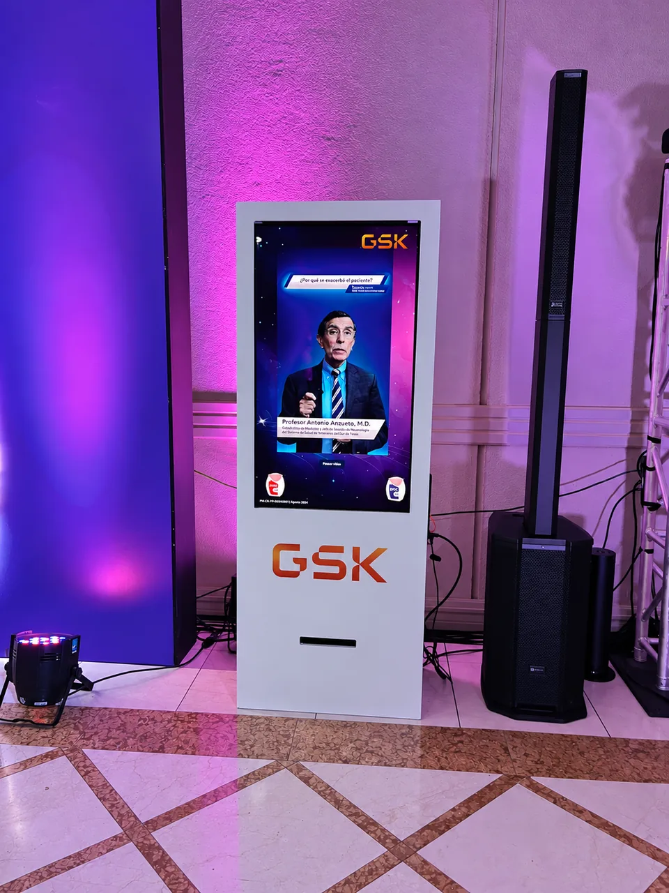 Tótem Interactivo con contenido audiovisual y gráfica GSK, junto a un altavoz en el evento