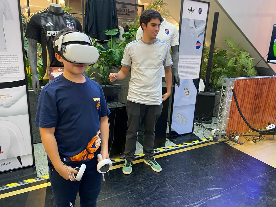 Participante usando un visor de realidad virtual y controles, acompañado por el equipo en una activación de Adidas