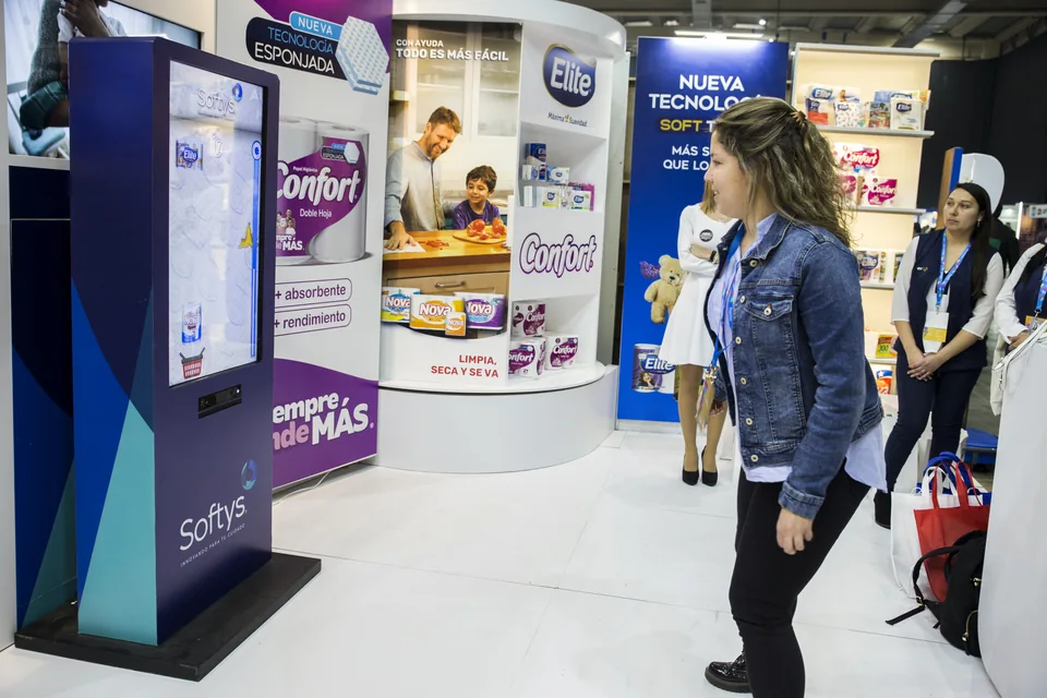 Tótem de MazeLab con gráfica de Softys y juego en pantalla, frente a una participante en el stand