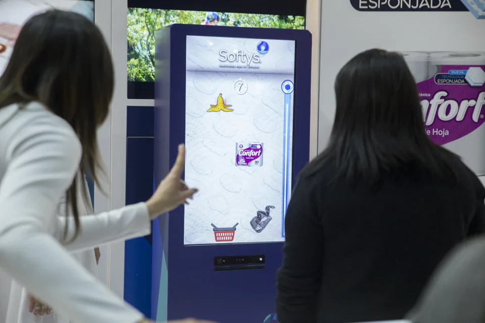 Dos asistentes frente al tótem de Softys, con el juego de productos visible en la pantalla
