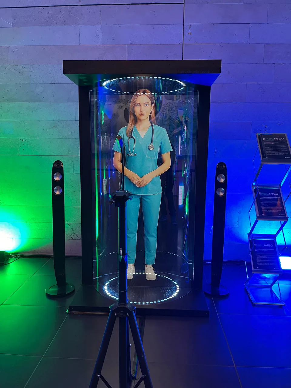 Tubo Holográfico con un personaje digital en pantalla y altavoces en un montaje real